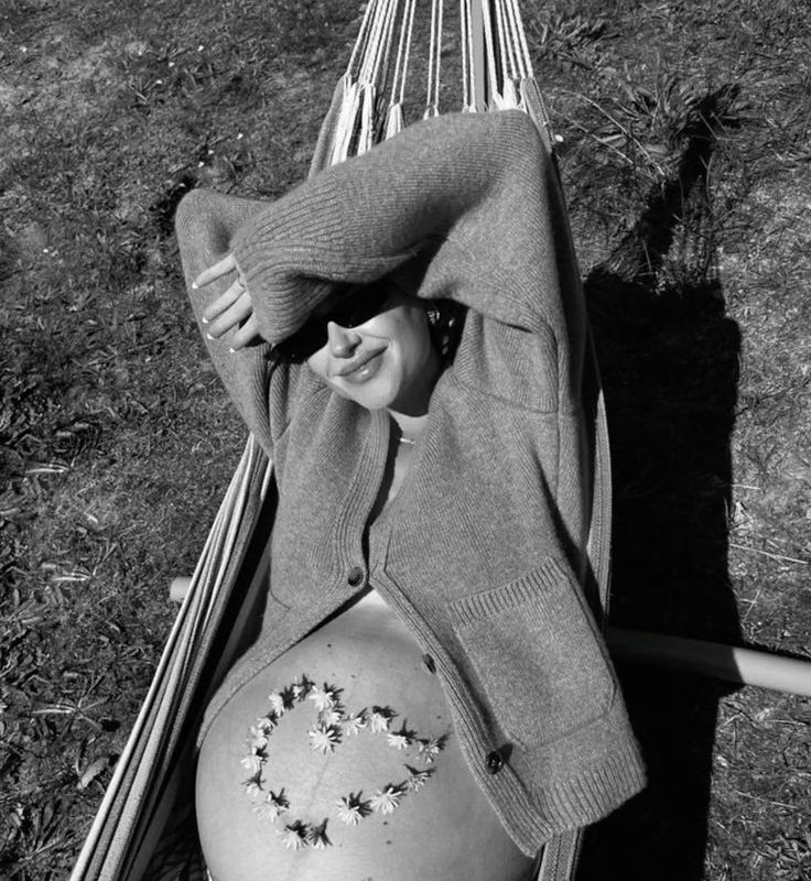 A pregnant woman relaxing in a hammock with flowers arranged in a heart on her belly, illustrating a guide to pregnancy-safe skincare by Body Sculpting Clinics Sydney.