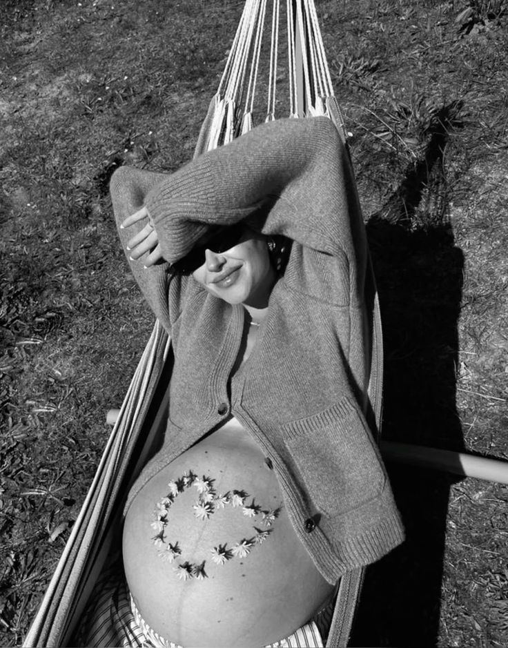 A pregnant woman relaxing in a hammock with flowers arranged in a heart on her belly, illustrating a guide to pregnancy-safe skincare by Body Sculpting Clinics Sydney.