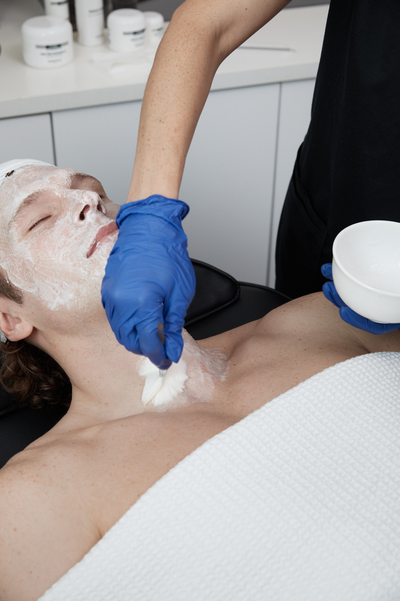 Clinician applying a DMK specialty treatment mask using a brush onto a male client's face and neck at Body Sculpting Clinics Sydney.